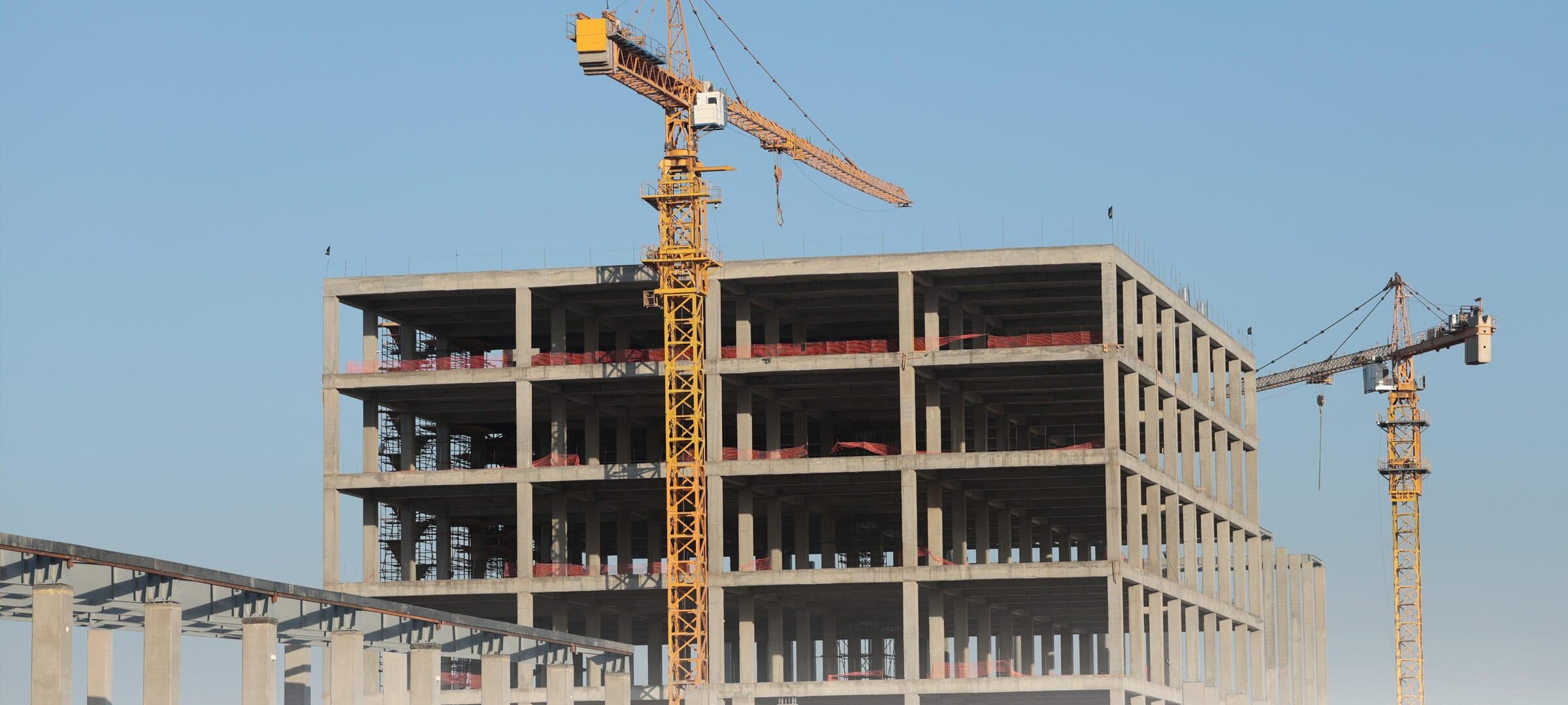 A multi-storey building under construction on the Diwan site, with two tower cranes beside it